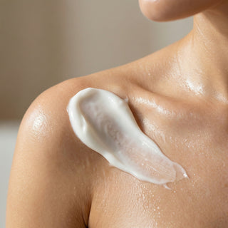 Close-up of a women applying cream to their shoulder with a neutral background